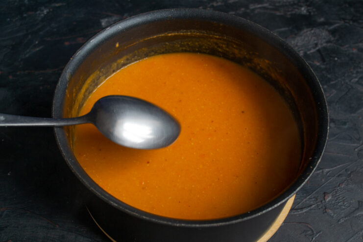 Using an immersion blender to create a smooth and creamy soup texture. Blending the cooked lentil soup in the pot with an immersion blender.