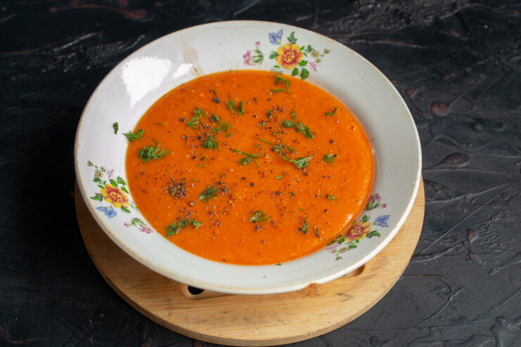 Serving the hot and delicious red lentil soup. Enjoy your meal! A bowl of hot red lentil soup, garnished with pepper and herbs, ready to be served.