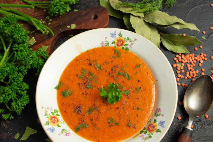 A bowl of finished vegetarian red lentil soup, garnished with herbs.