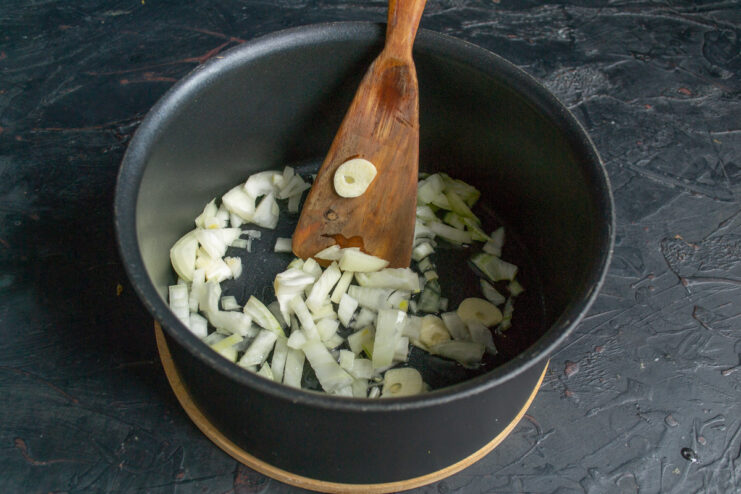Sautéing finely chopped onion and garlic in olive oil to build the soup's flavor base. Chopped onion and garlic being sautéed in a pot with olive oil.