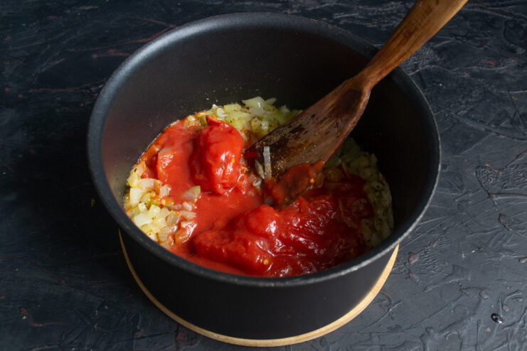 Adding peeled canned tomatoes to the sautéed vegetables. Peeled canned tomatoes being added to the pot of cooked vegetables.