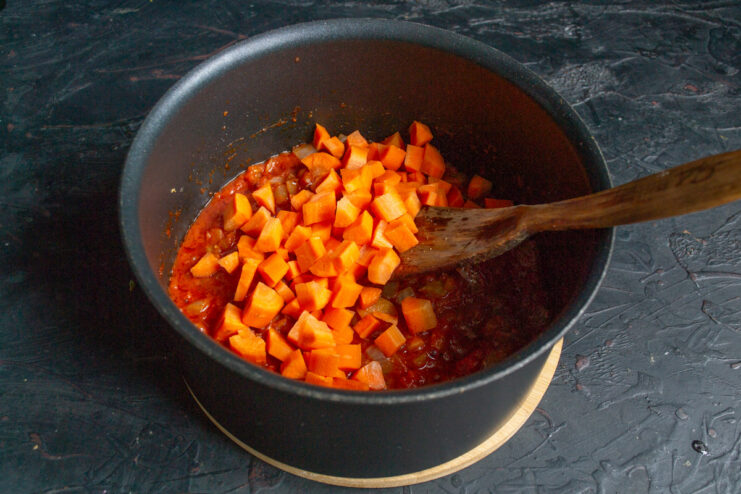 Adding diced carrots to the soup base. Diced carrots being added to the tomato and vegetable mixture in the pot.