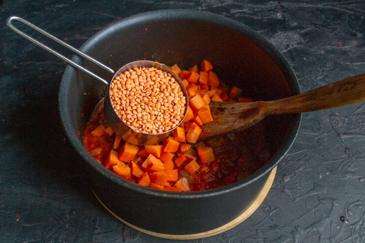 Adding rinsed red lentils to the pot. Dry red (orange) lentils being poured into the pot with vegetables.