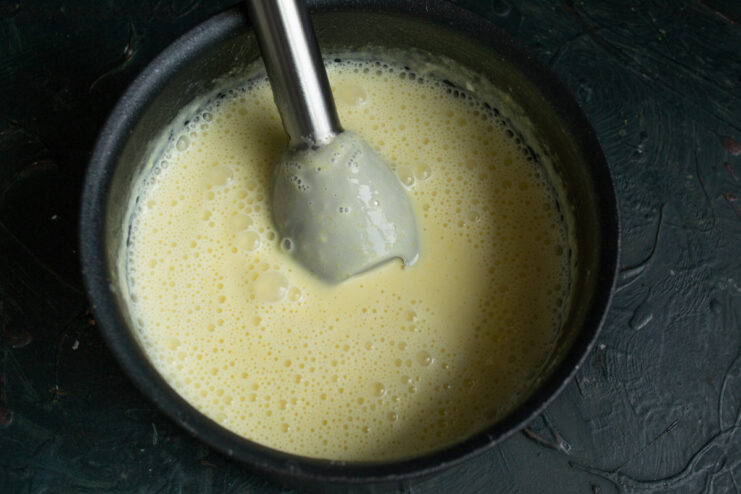 The final touch: add cream for a rich and luxurious finish Cream being poured into the blended zucchini soup in a pot.