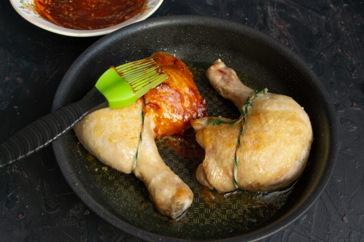 Brushing the Chicken with a Generous Layer of Homemade BBQ Glaze A cooking brush applying a thick, dark BBQ glaze onto the chicken.