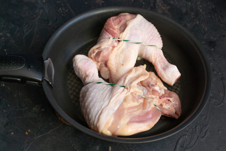How to Sear Chicken for a Crispy Skin Before Baking Raw chicken leg quarters being placed into a hot cast-iron skillet.