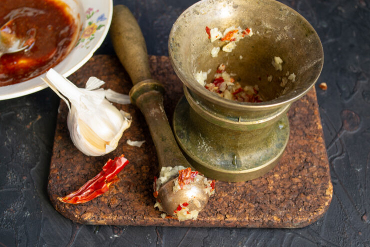 Preparing Fresh Chili and Garlic for the BBQ Sauce A mortar and pestle with garlic and deseeded chili pepper, ready for grinding.