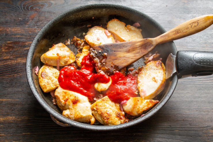 Adding Tomato Purée to Create the Sauce Tomato purée being added from a spoon into the pan with all ingredients.