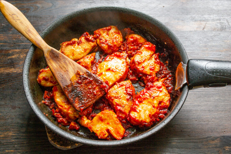 Adding a Pinch of Cinnamon for Aroma Sprinkling ground cinnamon over the chicken and tomato sauce in the pan.