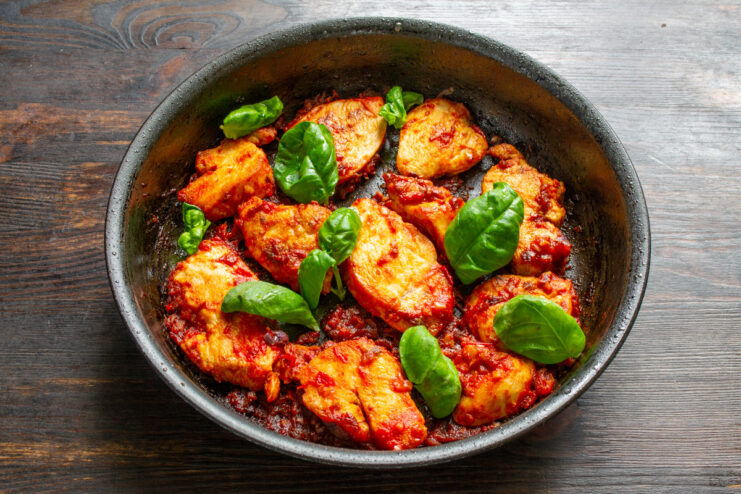 Final Dish Garnished with Fresh Basil The finished chicken in tomato sauce with dates in a pan, garnished with fresh basil leaves.