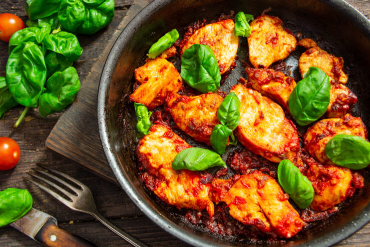 A plate of chicken breast in a rich tomato sauce with dates, garnished with fresh basil.