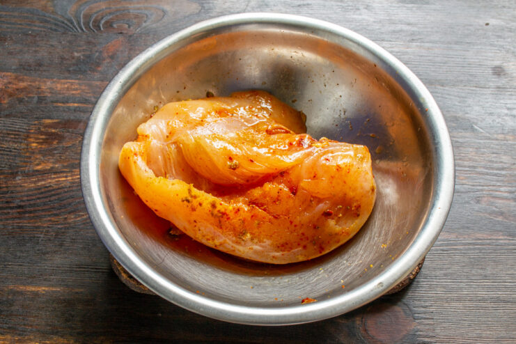 Marinating the Chicken Breast with a Spice Rub Raw chicken breast being rubbed with spices before being wrapped in plastic for marinating.