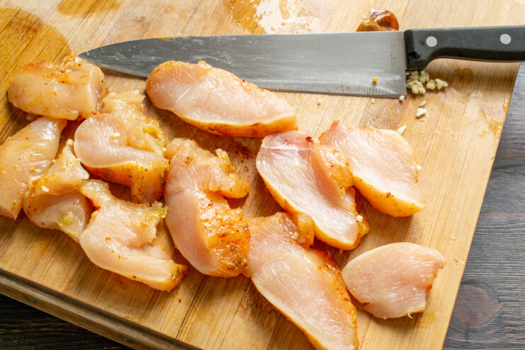 Slicing the Marinated Chicken Breast Marinated chicken breast being sliced into thick pieces on a cutting board.
