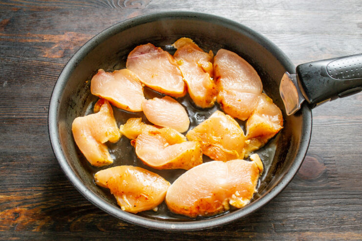 Searing the Chicken Pieces in a Hot Pan Sliced chicken pieces being placed into a hot frying pan with oil.
