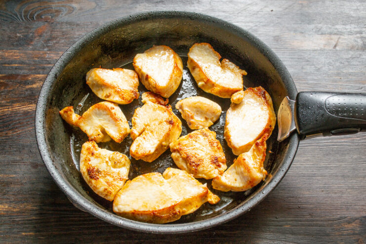 Frying Chicken Until Golden Brown Chicken pieces being pan-fried until they are a light golden brown color.