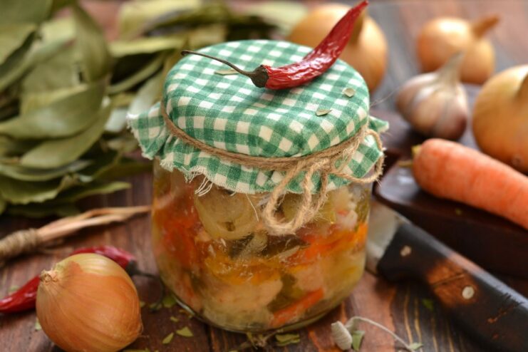 A glass jar filled with oven-baked chicken tushonka, showing pieces of chicken and vegetables.
