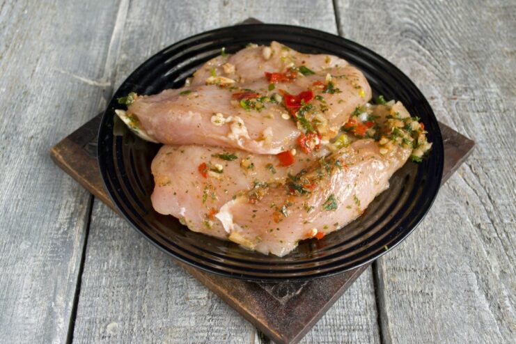 Marinating the chicken fillet is a key step for a juicy and flavorful result. Raw chicken fillet being coated in a green herb and spice marinade in a bowl.