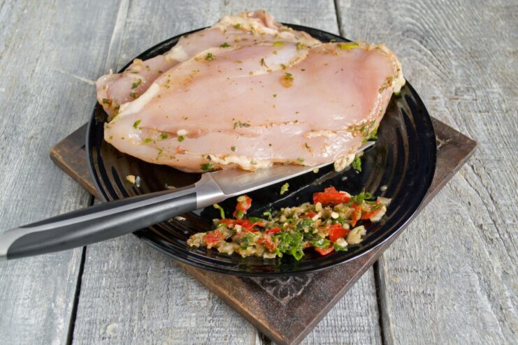 Scrape off the marinade before grilling to prevent it from burning. A hand using the back of a knife to scrape excess marinade off a chicken fillet.