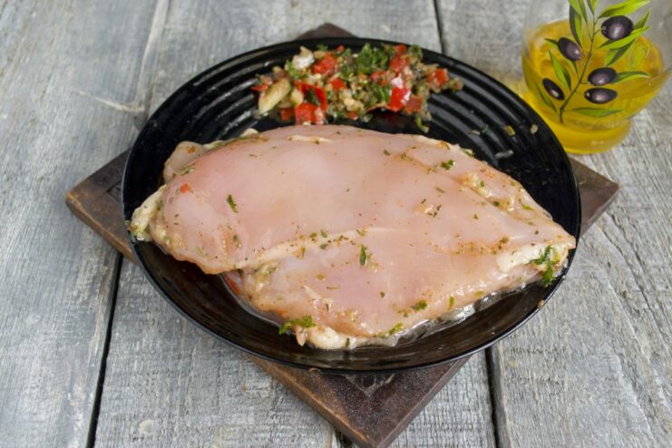 A light coating of olive oil helps to get perfect grill marks and prevents sticking. A hand rubbing olive oil onto a marinated chicken fillet before grilling.