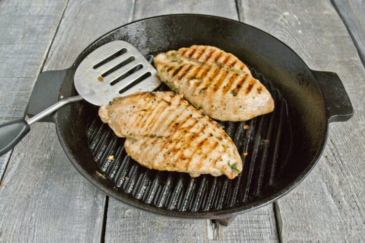 Grill for a few minutes per side until cooked through and grill marks appear. A chicken fillet cooking on a hot grill pan, showing prominent grill marks.