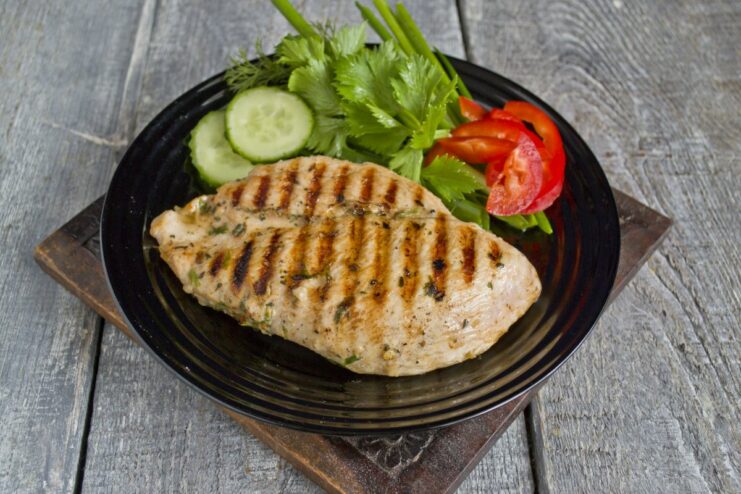 Serve the juicy grilled chicken with a fresh salad for a complete and healthy meal. A sliced grilled chicken fillet served on a plate with fresh vegetables and herbs.