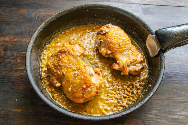 Baking the Chicken Thighs in the Oven to Finish Cooking A skillet with chicken thighs in sauce being placed into a hot oven.