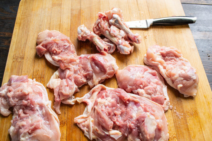 Preparing Chicken Thighs by Removing the Bones Raw chicken thighs on a cutting board, one being deboned with a knife.