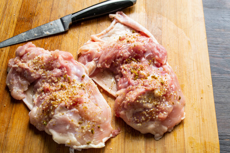 Seasoning the Chicken Thighs with Salt and Pepper Hand rubbing salt and pepper into boneless, skin-on chicken thighs.
