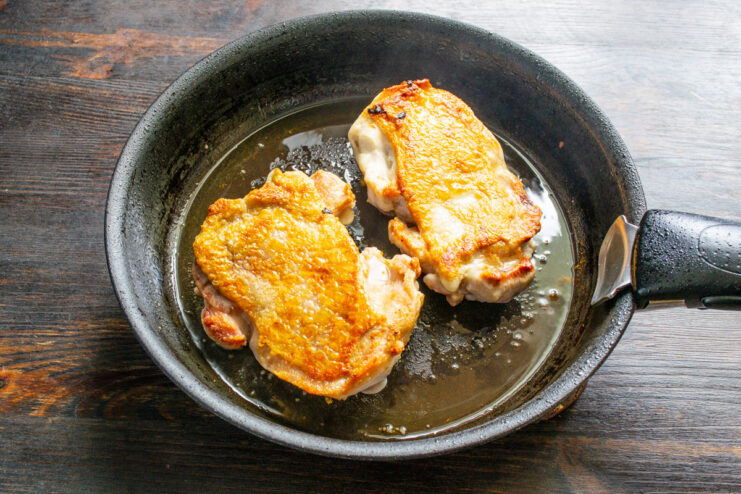Flipping the Chicken Thighs to Brown the Other Side Golden-brown, crispy-skinned chicken thighs being flipped over in a skillet.