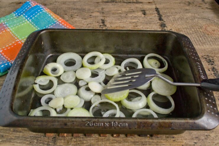 Sliced raw onions arranged in a single layer at the bottom of a glass baking dish.