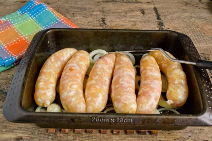 Raw chicken sausages placed in a single layer over a bed of sliced onions in a baking dish.