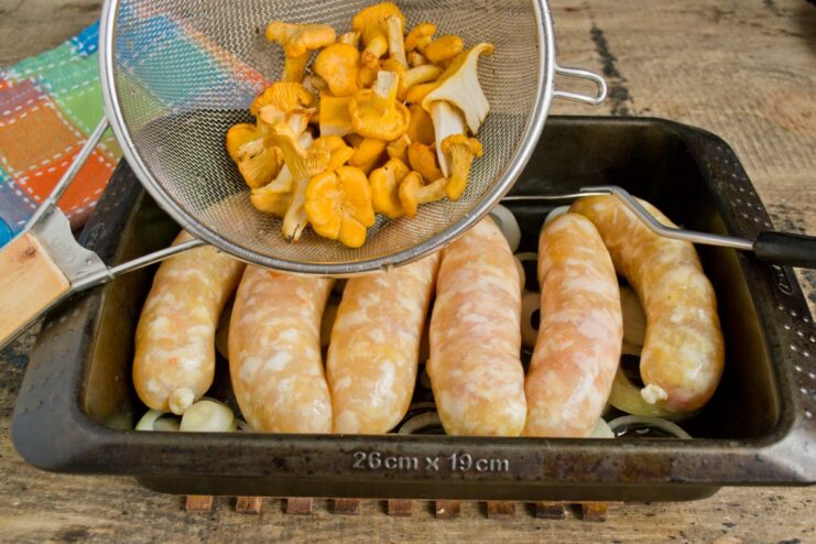 Fresh chanterelle mushrooms being added to the baking dish with chicken sausages and onions.