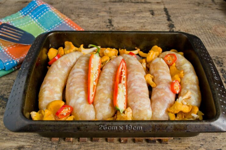 Sliced chili peppers added to the baking dish with sausages and mushrooms.