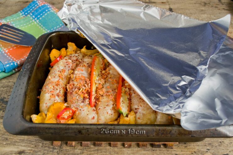 A glass baking dish filled with ingredients being tightly covered with aluminum foil.