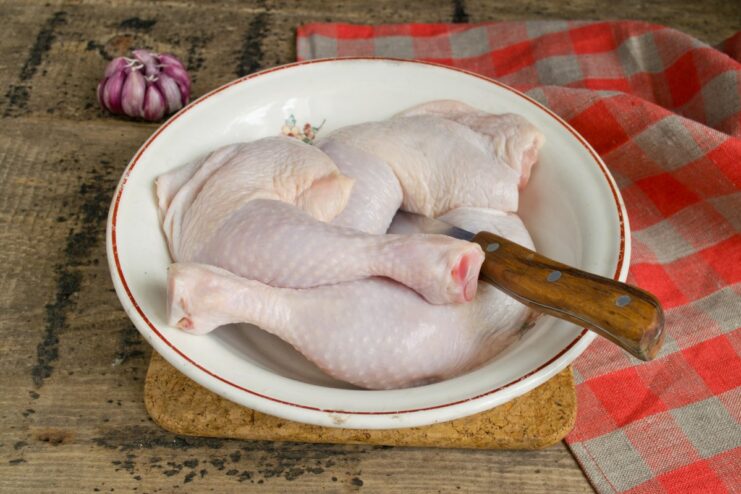 Step 1: Rinsing chicken legs under running water Raw chicken leg quarters being rinsed with water in a kitchen sink before cooking.