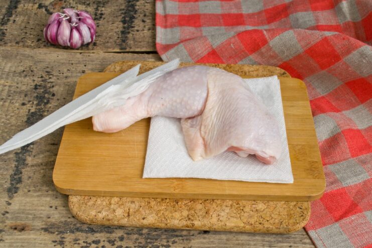 Step 2: Drying the chicken is key for crispy skin A hand patting raw chicken legs dry with a white paper towel to remove excess moisture.