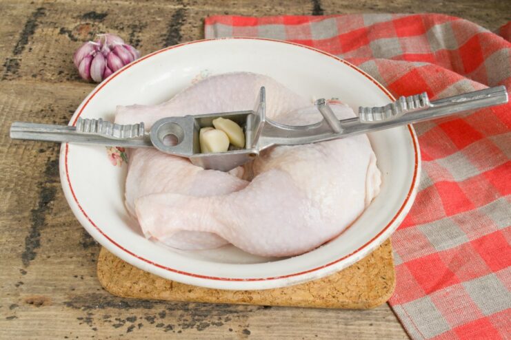 Step 4: Infusing flavor by putting garlic under the skin A hand rubbing minced garlic under the skin of a raw chicken leg for extra flavor.