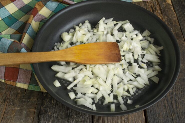 Sautéing Onions for the Sauce Base Finely chopped onions being sautéed in butter in a black frying pan until translucent.