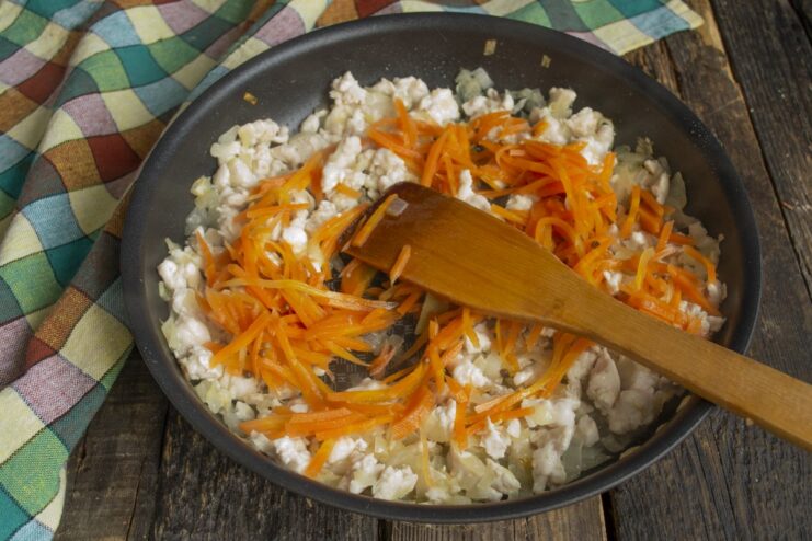 Adding Carrots to the Chicken and Onions Grated carrots being added to the frying pan with cooking chicken and onions.