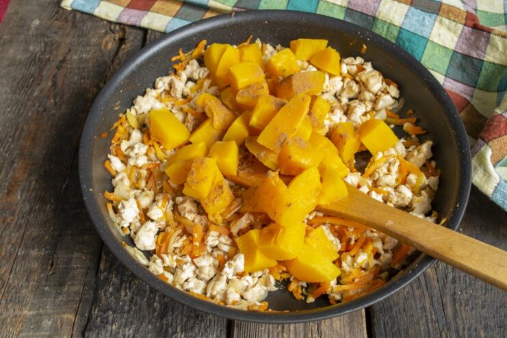 Combining Cooked Pumpkin with Chicken and Spices Cooked pumpkin pieces being added to the pan with chicken and sprinkled with cinnamon.