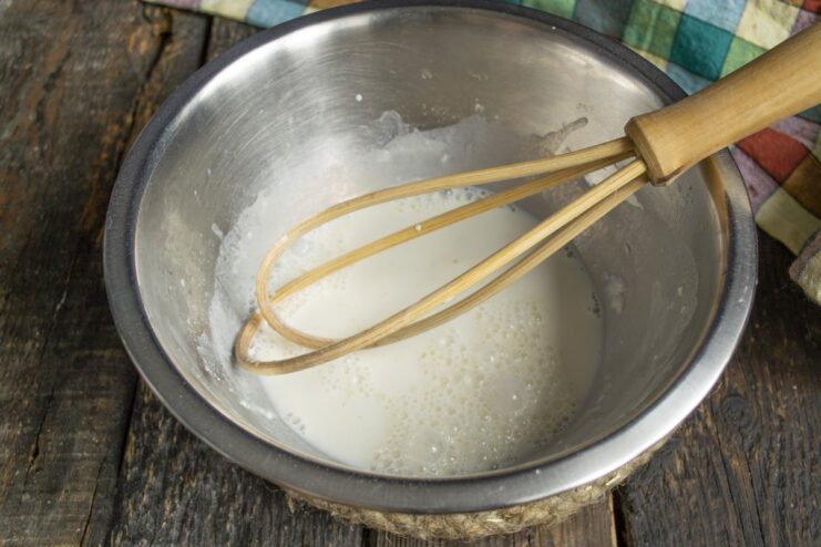 Preparing the Creamy Milk Sauce with a Whisk Whisking flour and milk in a glass bowl to create a smooth, lump-free sauce base.