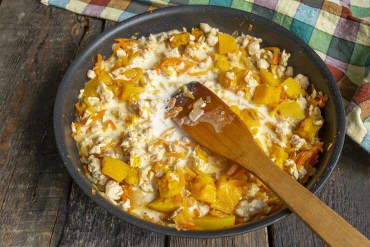 Thickening the Sauce with Chicken and Pumpkin Pouring the creamy milk sauce from a bowl into the pan with chicken and pumpkin.