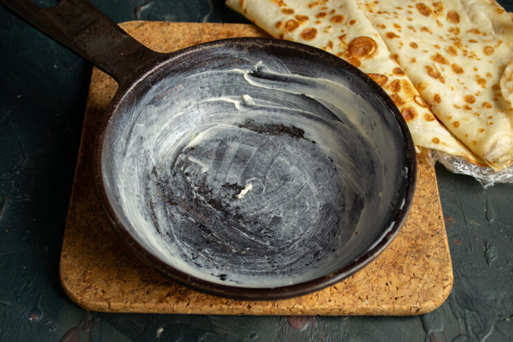 A hand greasing a deep baking dish with a piece of butter.