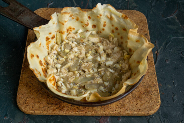 A portion of the savory filling spread over a pancake layer in the baking dish.