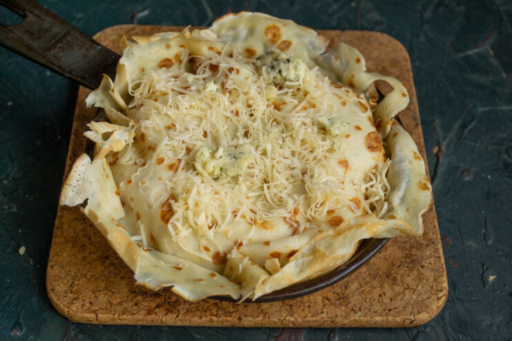 Grated cheese being sprinkled over the top of the assembled pancake pie before baking.