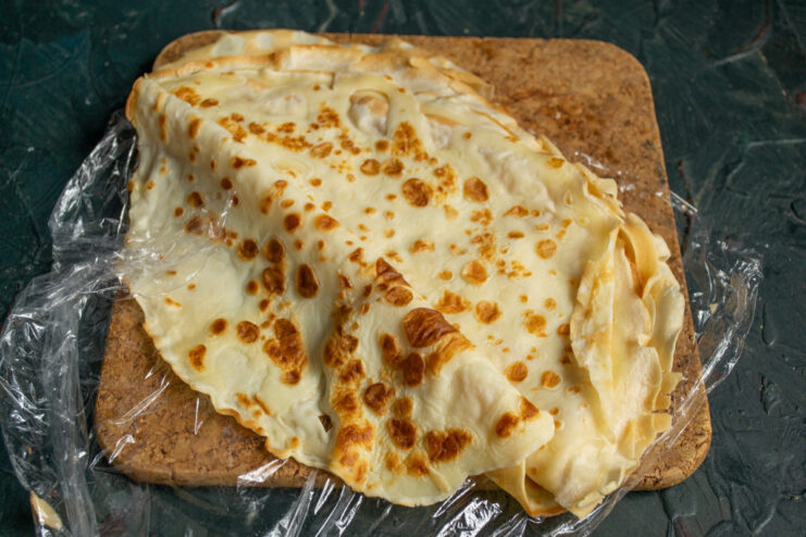 A thin pancake, or blin, being cooked in a black frying pan.