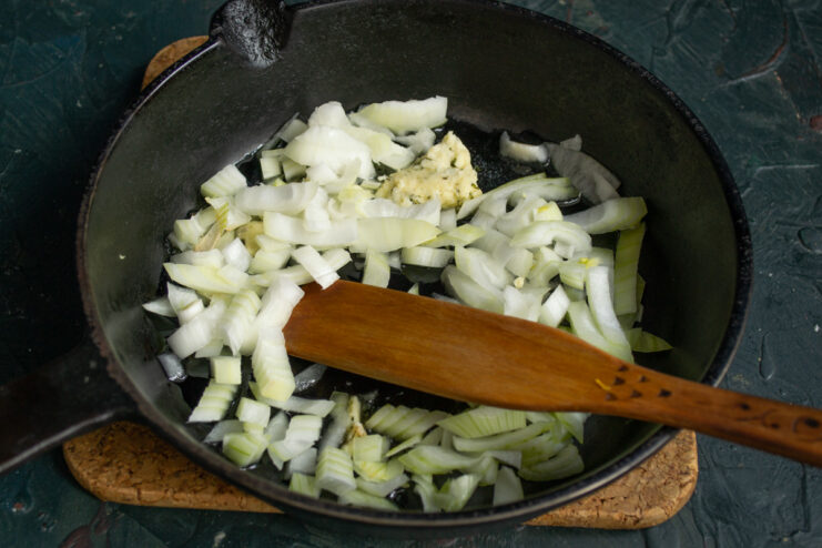 Chopped onions being sautéed in a pan until soft.