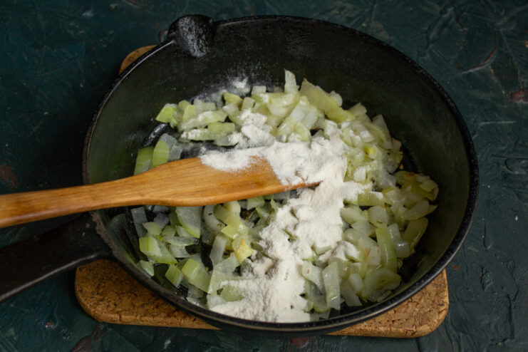 Flour being stirred into sautéed onions in a pan to make a roux.