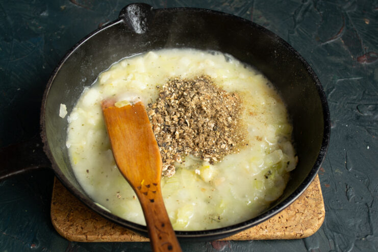 Mushroom powder being added to the onion and flour mixture in a pan.