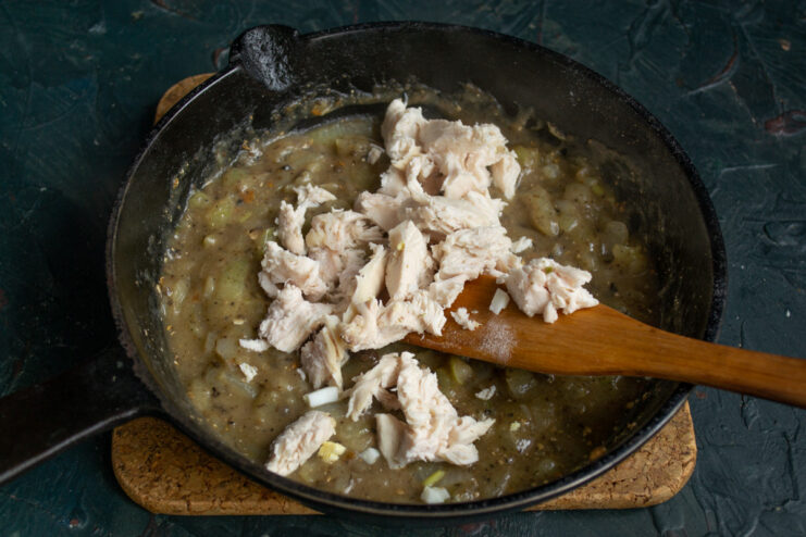 Chopped cooked chicken being added to the sauce in the pan.
